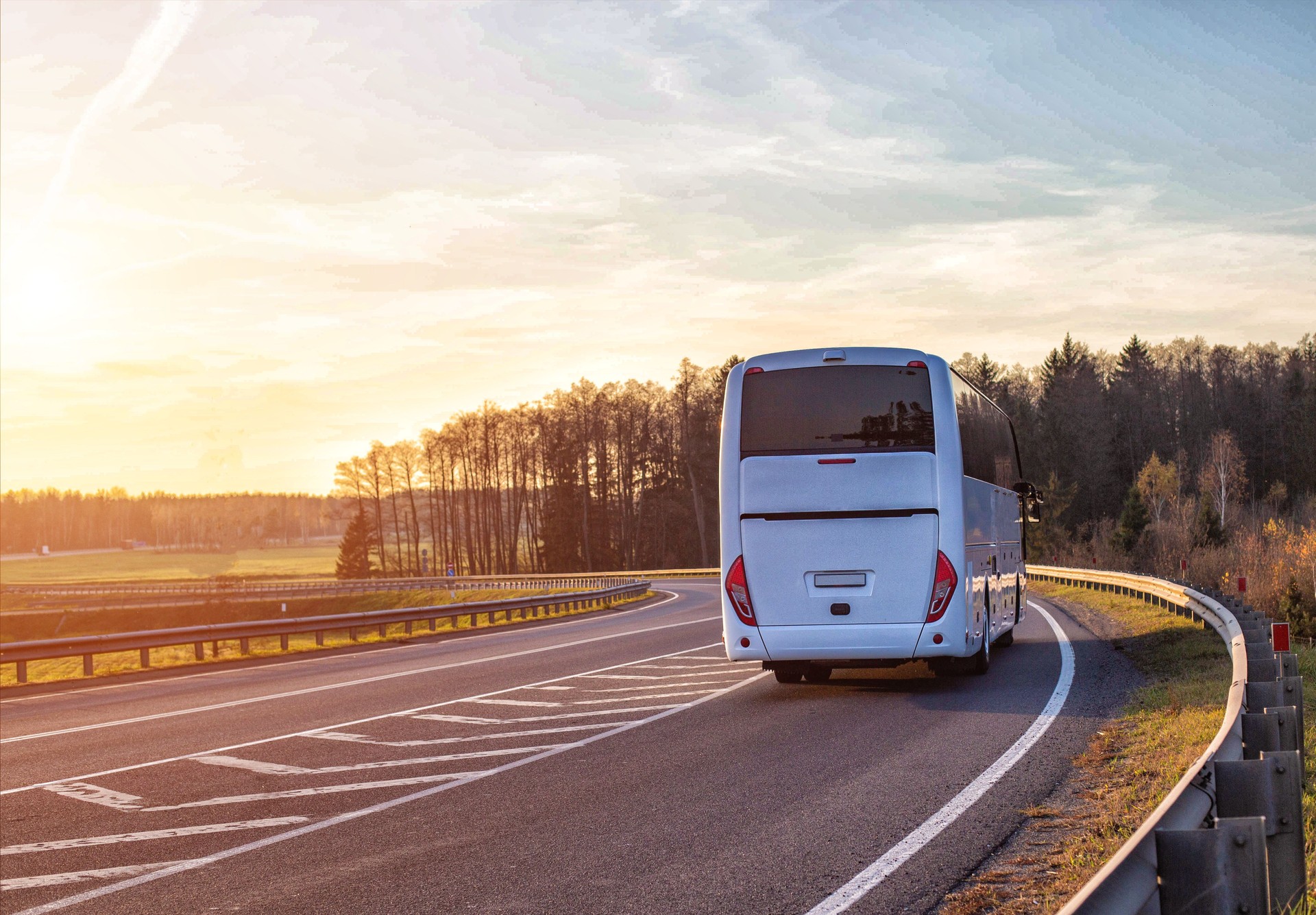A passenger bus travels along the highway against the backdrop of a forest and a sunset in the sky. Passenger transportation concept, safety and comfort, copy space for text