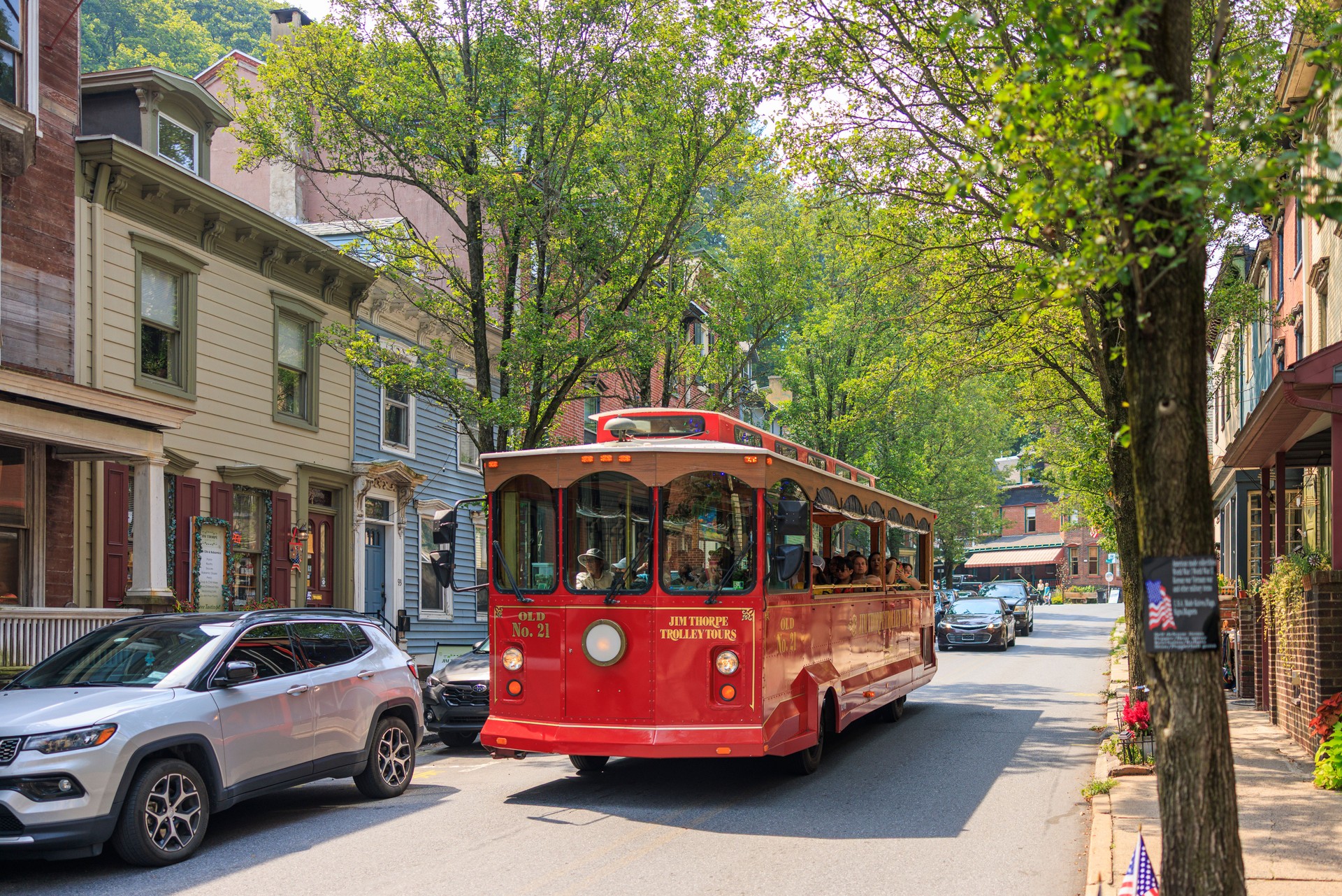 Trolley tour navigating tree-lined street between colorful buildings. Heritage tourism experience in small-town Pennsylvania.
